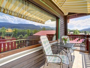 A balcony with a table and chairs, a view of a mountain landscape, and a wooden cabin structure. - 14th Floor With Panoramic Balcony and Lake View (Arrach)