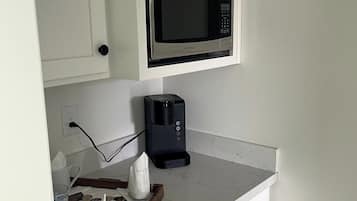 A kitchenette with a microwave, coffee maker, and a tray with cups and a teapot.