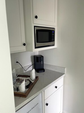 A kitchenette with a microwave, coffee maker, and a tray with cups and a teapot. - El Balcón  — Historic Pensacola Charm with a Private Balcony (Pensacola)