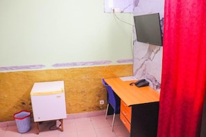 Ein kleines Zimmer mit Schreibtisch, Stuhl und einem kleinen, weißen Schrank.