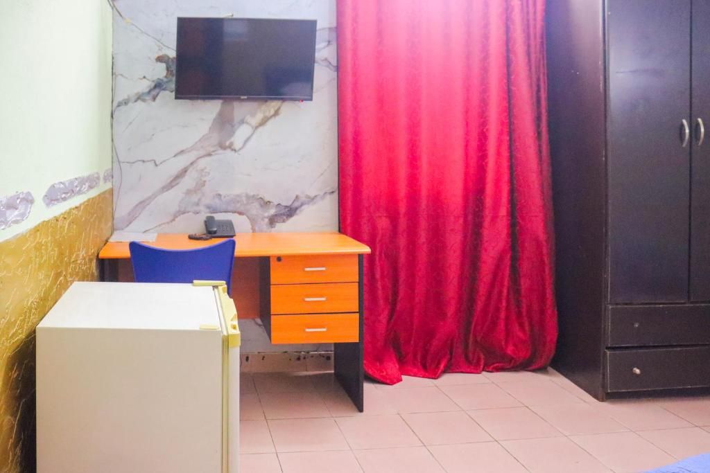 Una stanza con una scrivania, una sedia, un armadio e un televisore fissato al muro.