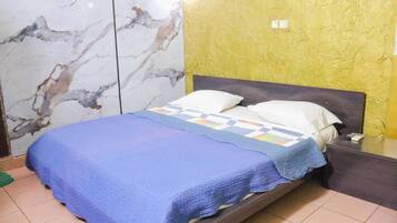 A bed with a blue blanket and pillows, a marble-patterned wall, and a yellow textured wall.