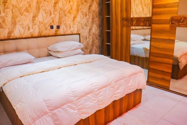 A bed with a headboard, a wall with a textured pattern, and a mirror reflecting the room.