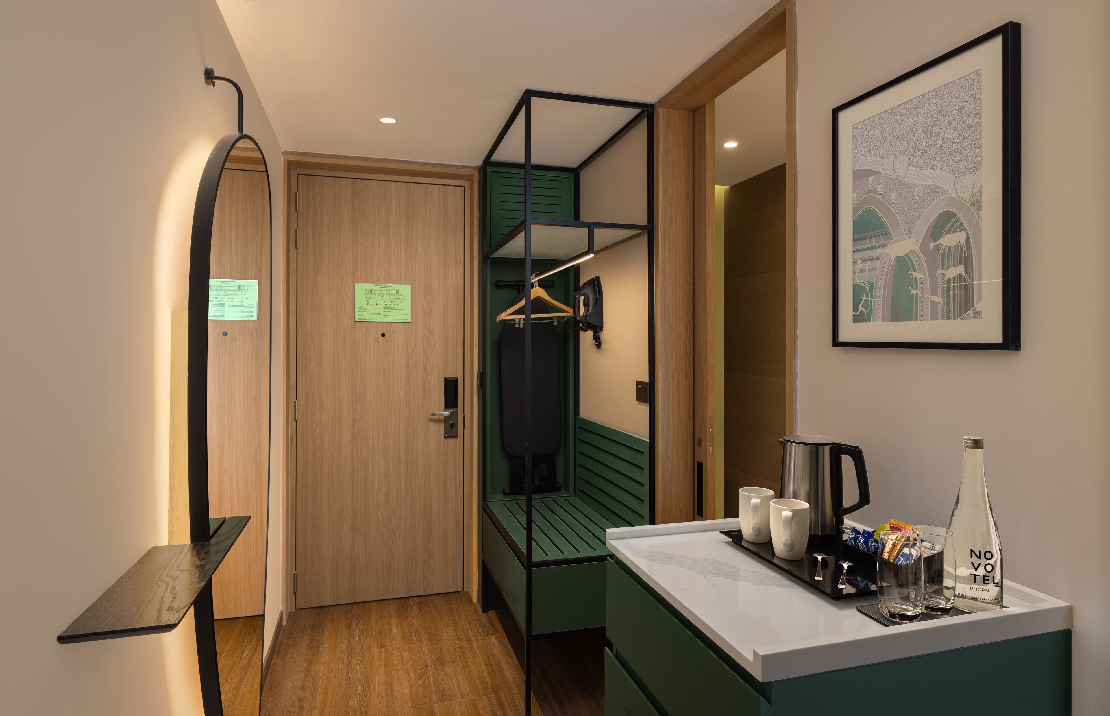 A compact hotel room with a bunk bed, a small kitchenette, a seating area, and a framed artwork on the wall.