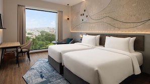 Ett hotellrum med två sängar, ett skrivbord, en stol och utsikt över staden, samt en vägg med ett mönster.