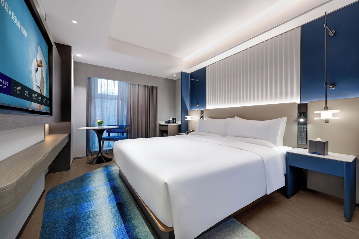Una habitación de hotel moderna con una cama grande, mesitas de noche, un escritorio y un televisor.