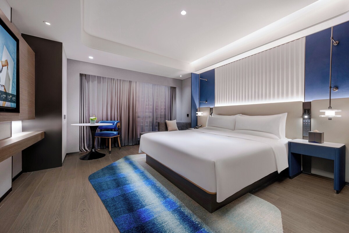 Una habitación de hotel moderna con una cama grande, mesitas de noche, un escritorio y una silla.