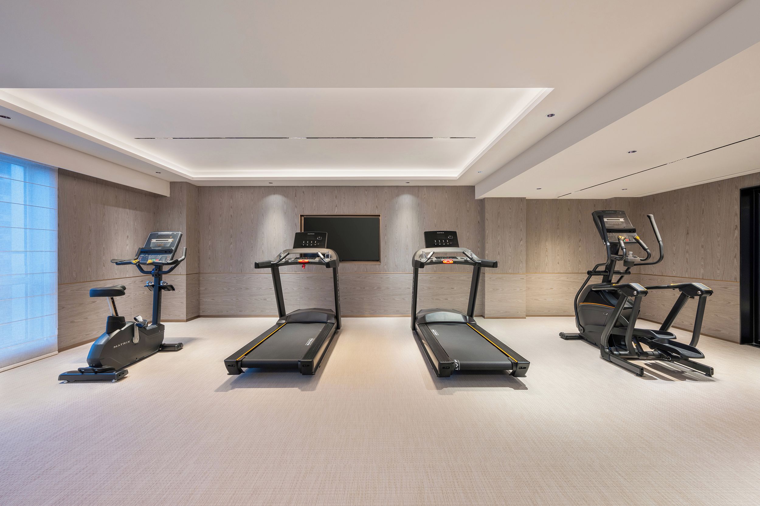 Une salle de sport moderne pour la maison, équipée de trois tapis de course, d’un vélo elliptique et d’un vélo d’appartement.