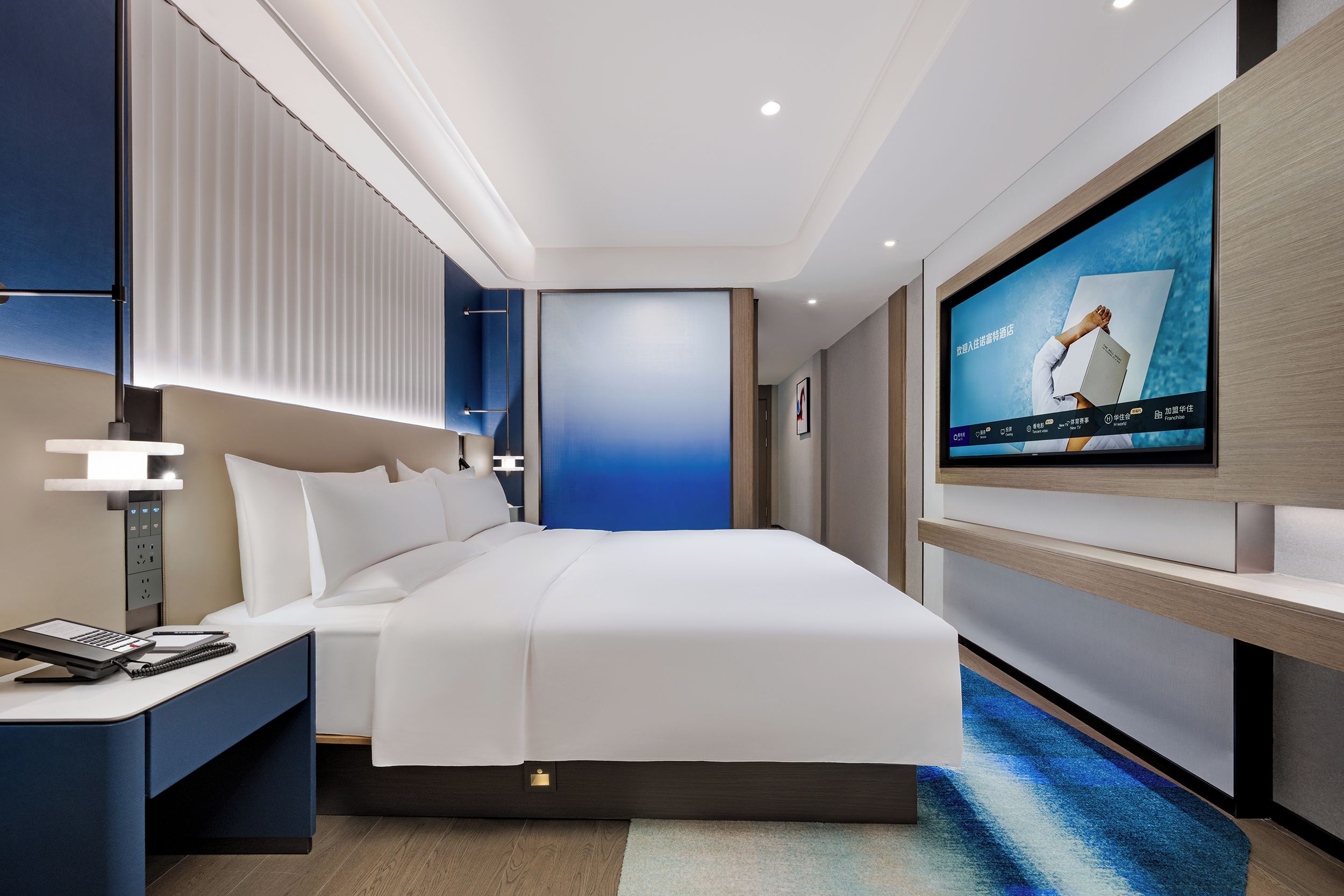 Une chambre d’hôtel moderne avec un grand lit, des tables de chevet, un téléviseur fixé au mur et un mur d’accent bleu.