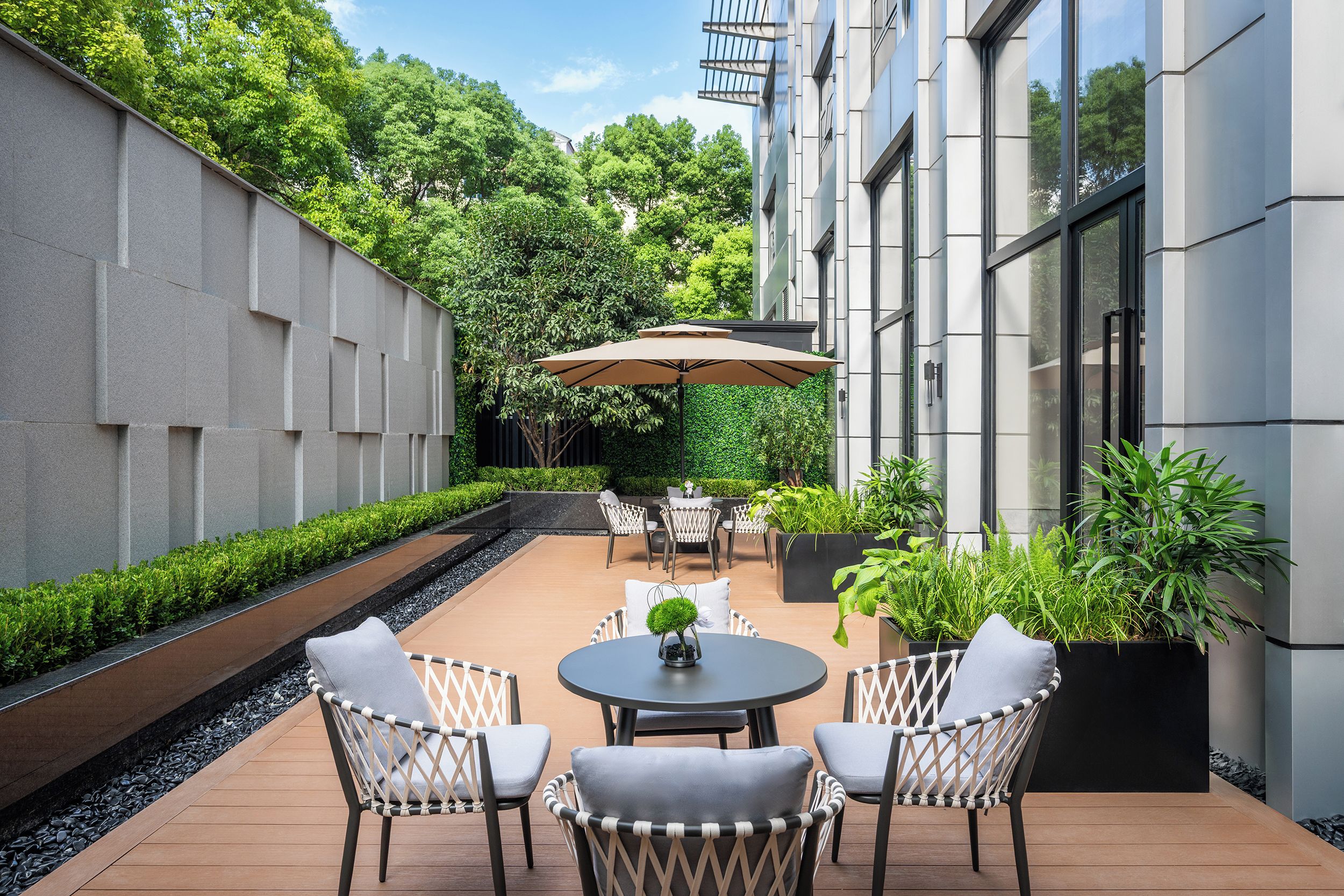 Un patio al aire libre con una mesa redonda y sillas, rodeado de follaje y un edificio moderno.