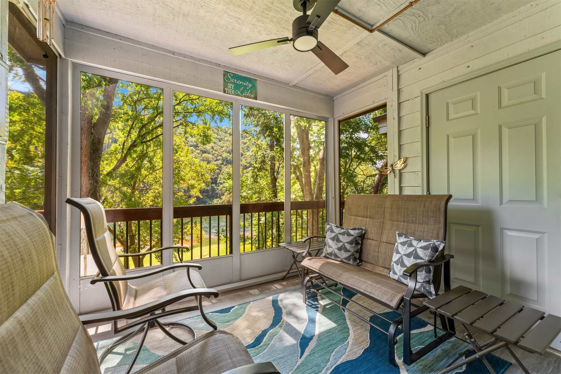 A sunroom with a view of trees and a ceiling fan.