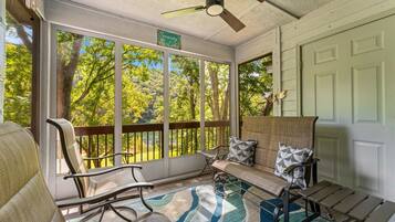 A sunroom with a view of trees and a ceiling fan.