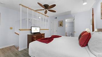 A hotel room with a bed, a ceiling fan, a TV on a dresser, and a door leading to a bathroom.