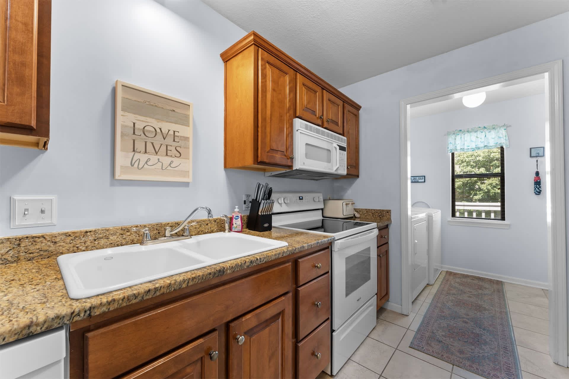 A kitchen with granite countertops, wooden cabinets, a white microwave, and a double sink.