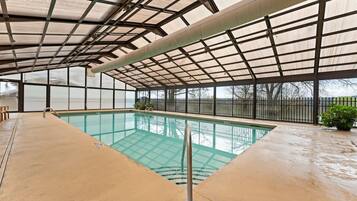 An indoor swimming pool with a glass ceiling, clear pool water, and a view of the outside.