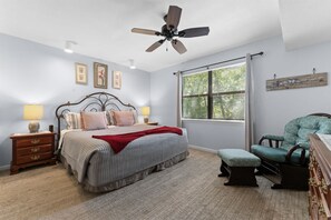A bedroom with a bed, nightstands, a chair, a window with blinds, and a ceiling fan. - Serenity by the Lake - 3BR Home (Branson)