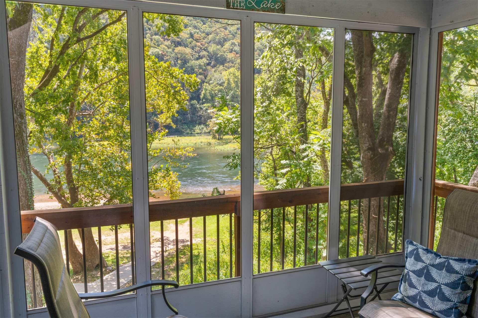 A covered porch with a view of a river and forest.