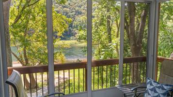 A covered porch with a view of a river and forest.