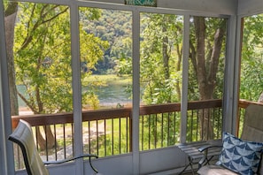 A covered porch with a view of a river and forest. - Serenity by the Lake - 3BR Home (Branson)