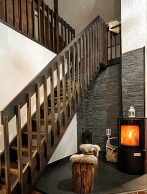 Eine Treppe mit hölzernen Geländern führt zu einer dunklen Steinwand. Auf der unteren Zwischenebene steht ein kleiner Tisch mit Kerze und Laterne.