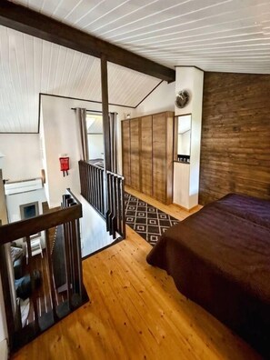 Ein Schlafzimmer mit Holzboden, einem Bett, einem Kleiderschrank und Blick auf einen Balkon.