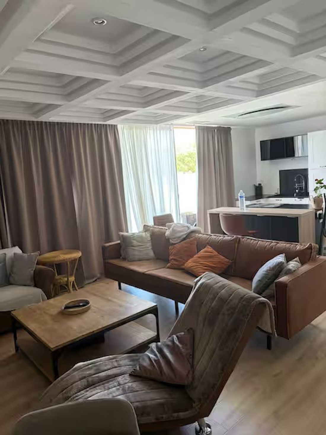 Ein modernes Wohnzimmer mit einer Couch, einem Sessel und einem Couchtisch. Es gibt eine Küchenzeile mit einem Fernseher und einem Spülbecken.