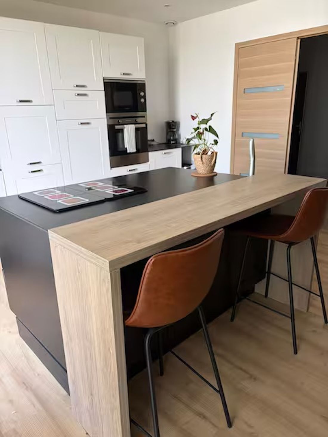 Eine moderne Küche mit weißen Schränken, einer schwarzen Arbeitsplatte und einer Holzeinsel mit zwei Stühlen.