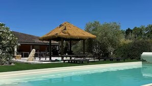 A swimming pool with a thatched-roof pavilion, a stone wall, and a grassy area. - Le Pignole · 2-bedroom apartment with AC and parking · Shared pool and garden · Sleeps 5 (Saint-Jory)