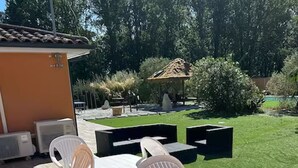 An outdoor patio with a table and chairs, a small building, and a well-maintained lawn. - Le Pignole · 2-bedroom apartment with AC and parking · Shared pool and garden · Sleeps 5 (Saint-Jory)