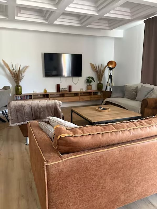 A modern living room with a sofa, a coffee table, a TV, and decorative plants. - Le Pignole · 2-bedroom apartment with AC and parking · Shared pool and garden · Sleeps 5 (Saint-Jory)