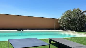 Ein Pool mit zwei Liegestühlen auf einer Rasenfläche.