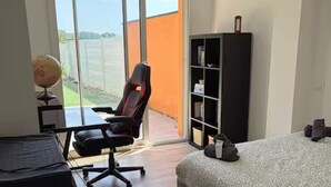 A bedroom with a bed, a desk, a chair, a bookshelf, and a sliding glass door leading to an outdoor area. - Le Pignole · 2-bedroom apartment with AC and parking · Shared pool and garden · Sleeps 5 (Saint-Jory)