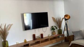 Een moderne woonkamer met een flatscreen televisie aan de muur, houten meubels en een plafond met geometrische patronen.