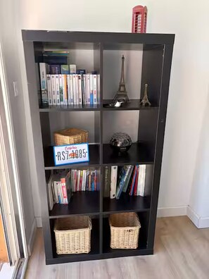 Une bibliothèque à plusieurs étagères, dont certaines sont remplies de livres et d’autres contiennent des objets décoratifs, comme des paniers et une petite maquette de la Tour Eiffel.
