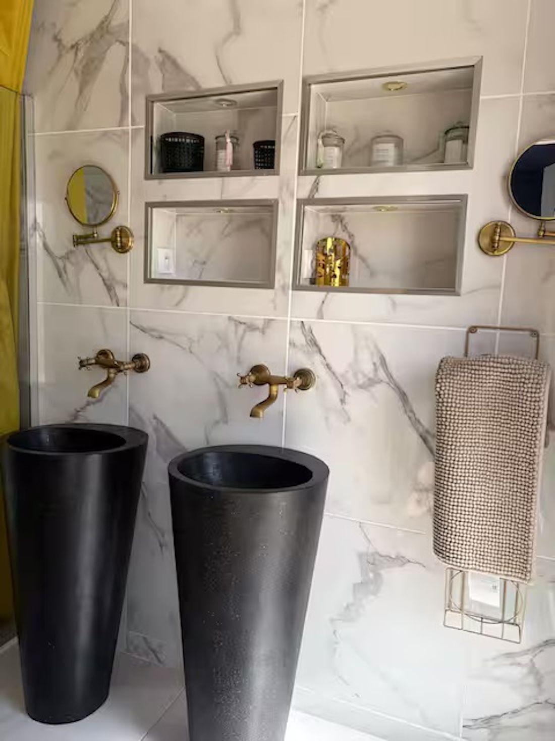 A bathroom with marble walls, two large black sinks, and shelves with toiletries.