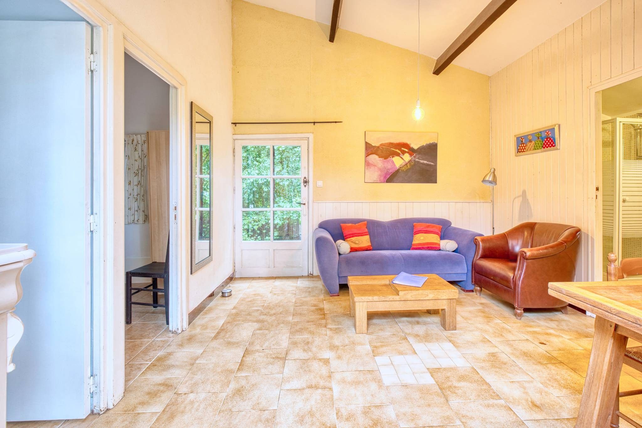 A room with a wooden floor, a sofa, a leather chair, a table, and a door leading to a balcony.