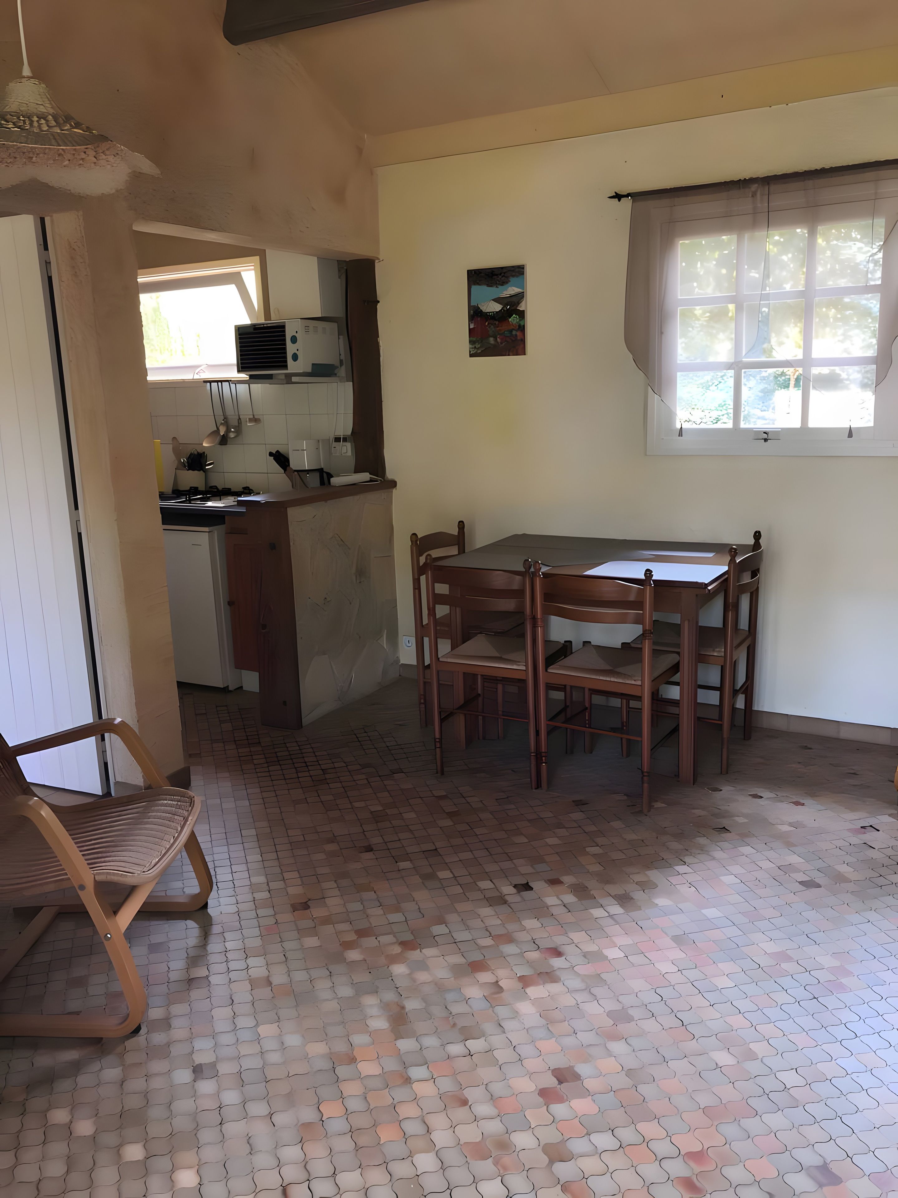 A kitchen with a dining table and chairs, a hanging light fixture, and a window with curtains.
