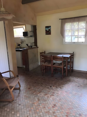 A kitchen with a dining table and chairs, a hanging light fixture, and a window with curtains.