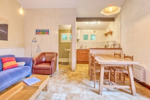 Una sala de estar acogedora con un sofá azul, un sillón de cuero marrón y una mesa de comedor de madera con sillas.