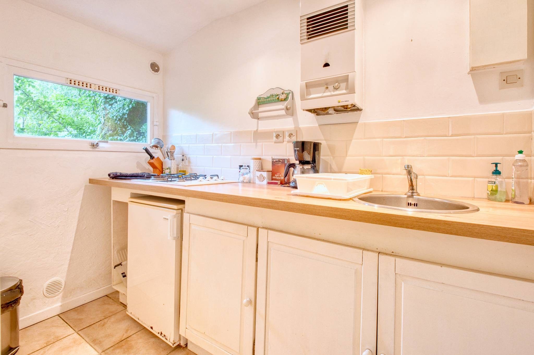 A kitchen with a window, a sink, a coffee maker, and cabinets.