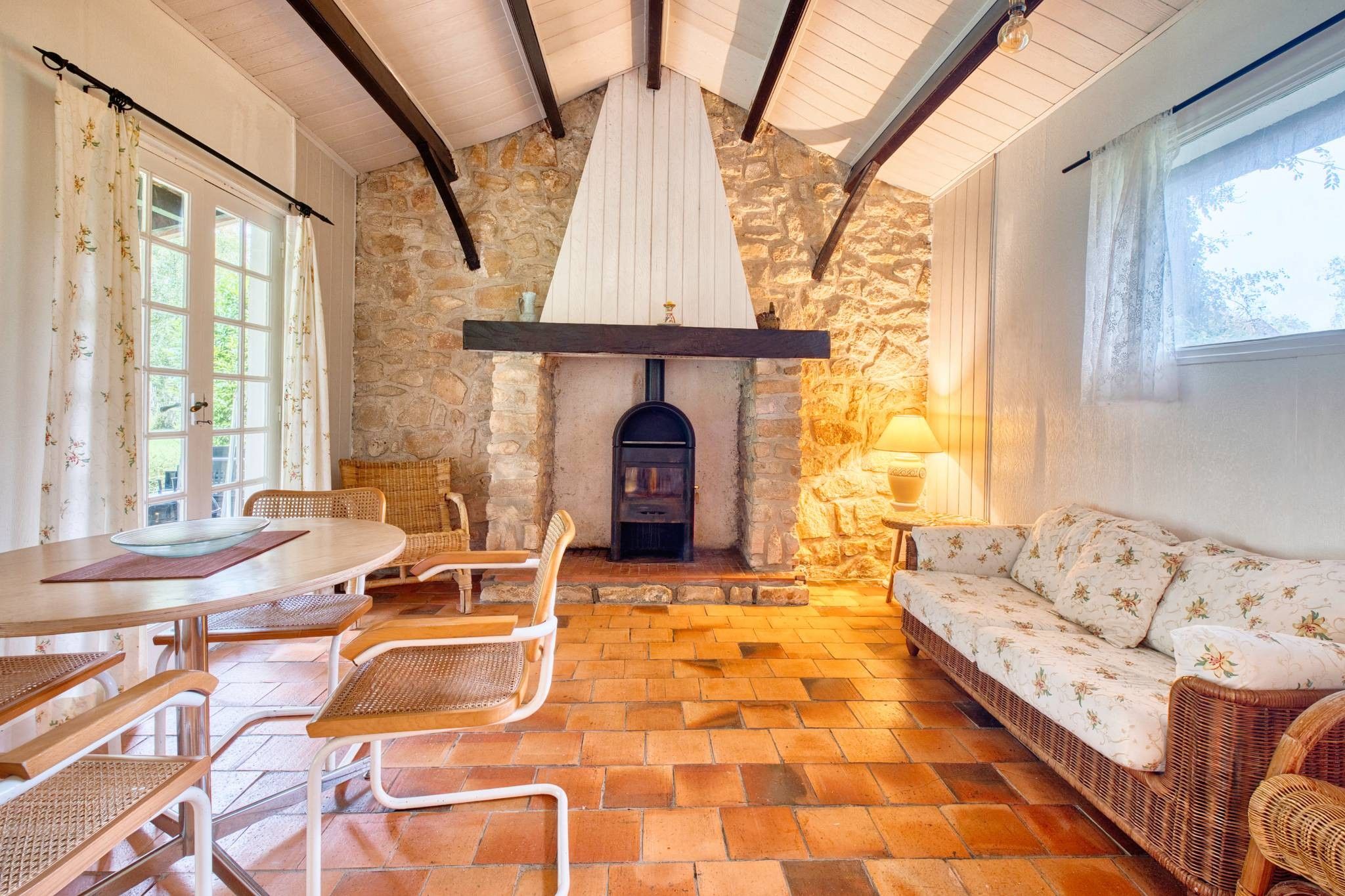 A cozy room with a stone wall, a fireplace, wicker furniture, and a table with chairs.