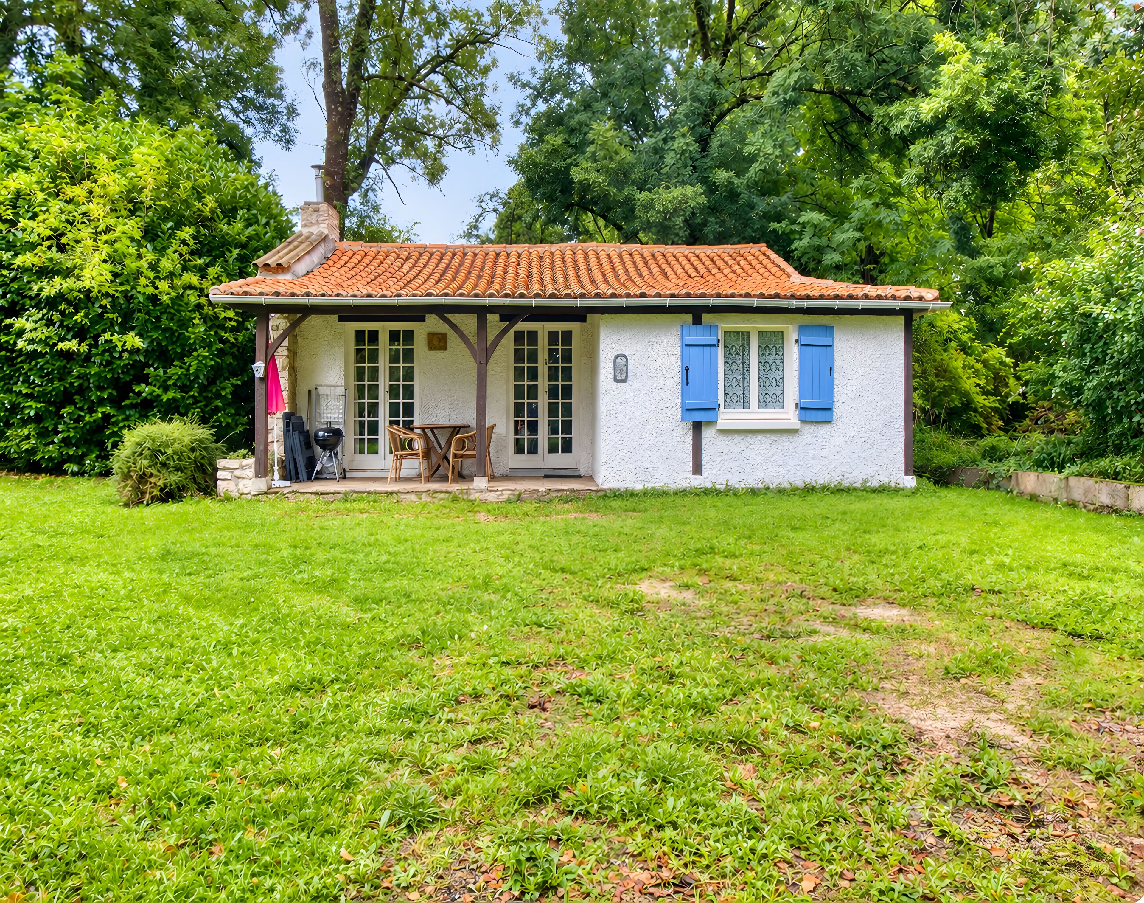 A small house with a tiled roof, a covered patio, and a well-maintained lawn.