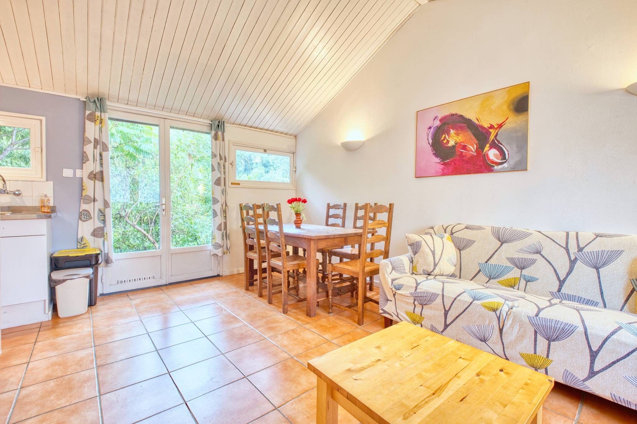A cozy living area with a wooden table, chairs, a sofa, and a painting on the wall.