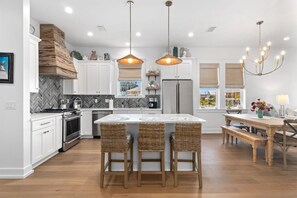 Eine moderne Küche mit weißen Schränken, einer zentralen Kochinsel mit Barhocker, einem eingebauten Ofen und einem Kühlschrank.