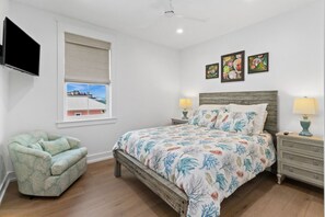 Ein Schlafzimmer mit einem Bett, einem Sessel, einem Fernseher, einem Fenster mit Jalousien und Bildern an der Wand.