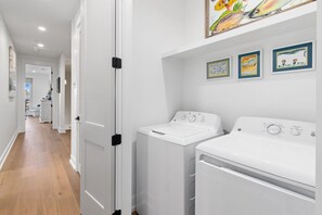 Een wasserette met twee witte wasmachines, een deur met zwarte handgrepen en drie ingelijste kunstwerken aan de muur.