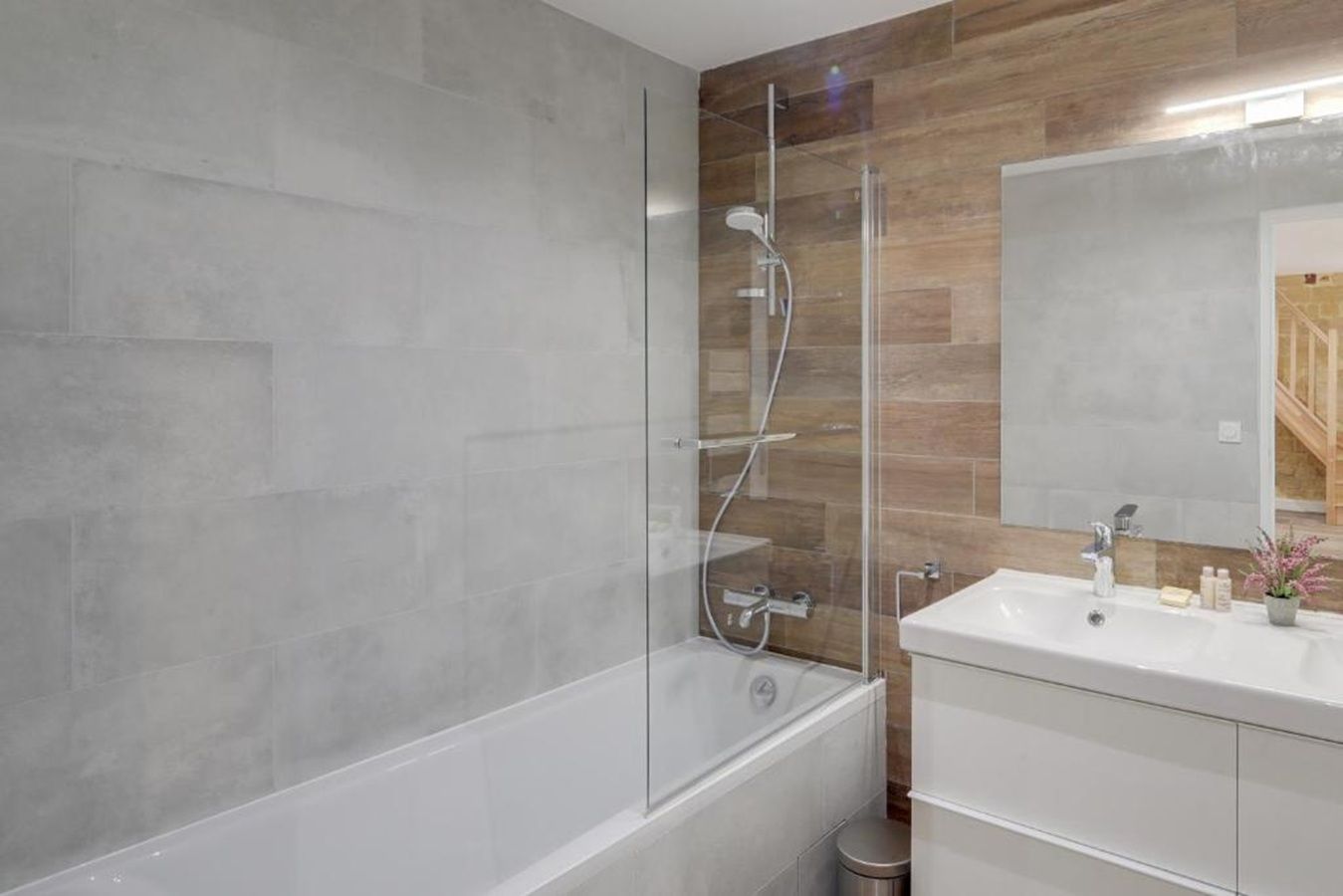A modern bathroom with a glass-enclosed shower, a white bathtub, and a vanity with a mirror.
