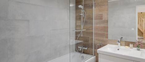 A modern bathroom with a glass-enclosed shower, a white bathtub, and a vanity with a mirror.