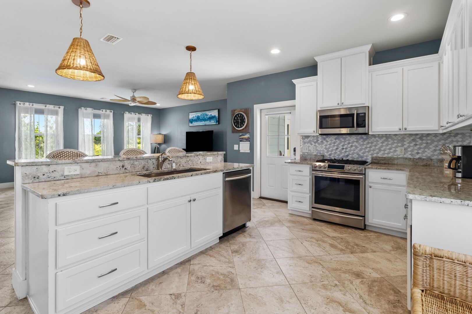 A modern kitchen with white cabinetry, a large island, stainless steel appliances, and pendant lighting.