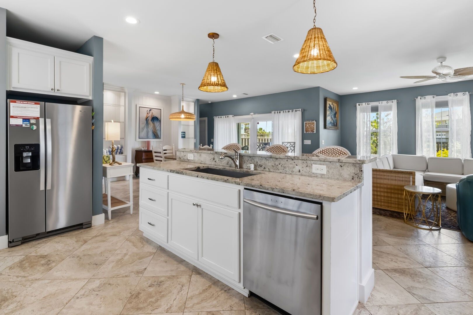 A modern kitchen with a stainless steel refrigerator, white cabinetry, a granite countertop, and a built-in dishwasher.